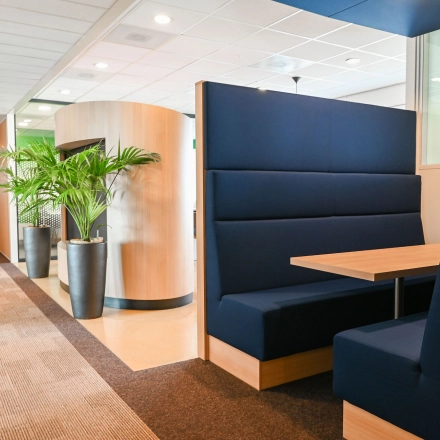 Modern office space at Weena 70, Rotterdam Center featuring stylish blue seating booths ideal for meetings, beside lush green plants. Perfect for those seeking office space rental options.