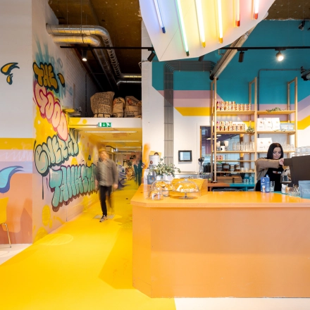 Vibrant interior at Weena 70, Rotterdam Center, featuring colorful decor and a café area where a person is preparing a beverage, ideal for office space rental.