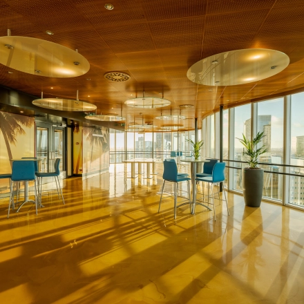 Bright office space rental at Weena 70, Rotterdam Center, featuring tall windows, modern decor, and bar-height tables with blue chairs, overlooking cityscape.