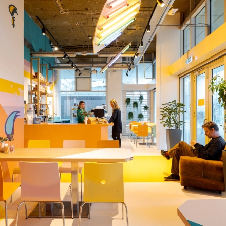 Lively office space at Weena 70, Rotterdam Center featuring a vibrant meeting and work area with people discussing and another person sitting. Ideal for office space rental.