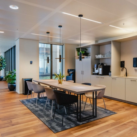 Modern office space at Weena 788, Rotterdam Center, featuring a furnished workspace with a long table, chairs, and kitchen facilities, ideal for office space rental.