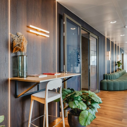 Stylish office at Weena 788 in Rotterdam Center featuring modern wooden accents, greenery, and a compact workspace ideal for rent. A person is seen engaging in business activities in the background.