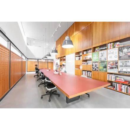 Spacious office space rental at Hofplein 20, Rotterdam Central Station, featuring a long table and shelves with books, ideal for collaborative work. Modern lighting and seating enhance the functionality.