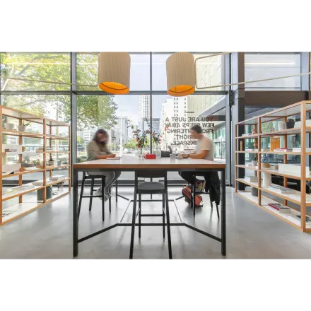 Modern workspace at Rotterdam Central Station featuring large windows, natural light, and individuals collaborating at a high table with shelving units around.
