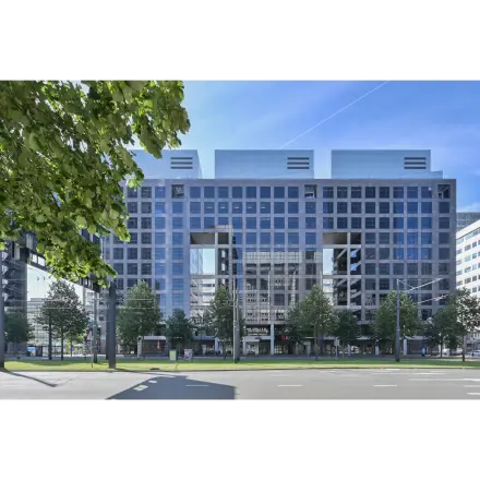 Exterior view of office space rental at Weena 290, Rotterdam Central Station, showcasing a modern building facade with large glass windows and surrounding greenery.
