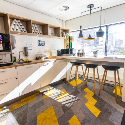 Bright and modern pantry at Weena-Zuid 130, Rotterdam Central Station, featuring a coffee machine, bar stools, and ample storage. Ideal spot in office space rental.