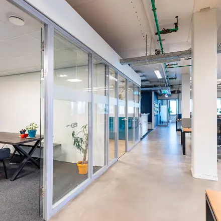 Modern office space at Kratonkade 7-27, featuring clear partitions, lounge chairs, and workstations, ideal for office space rental in Rotterdam Delfshaven.