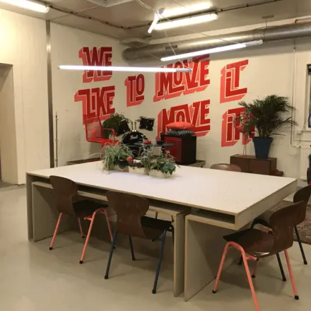 Interior view of a stylish office space with modern furnishings at Van Helmontstraat in Rotterdam Delfshaven, showing a large table with chairs, plants, and vibrant wall art.
