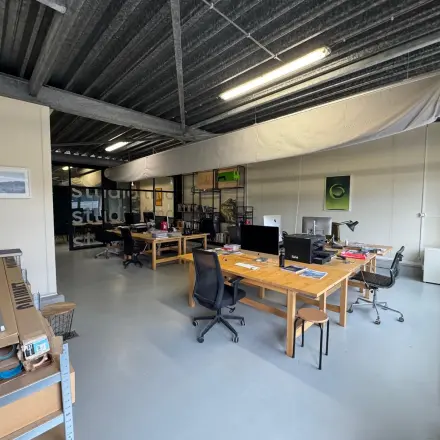 Interior view of a furnished office space at Van Helmontstraat 17-23 in Rotterdam Delfshaven, showcasing wooden desks and modern office chairs available for rent.