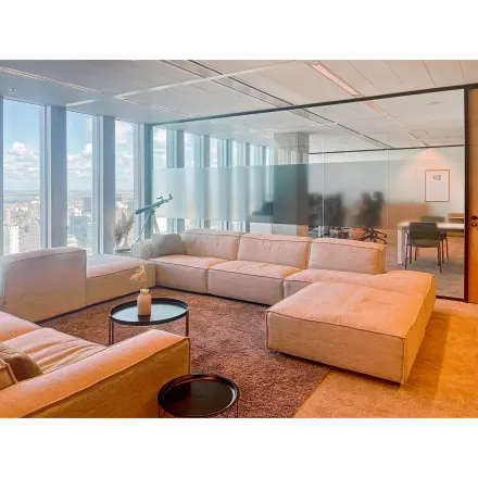 Spacious office lounge with comfortable seating and large windows offering a view of Rotterdam. Ideal for relaxing in a rented office space.