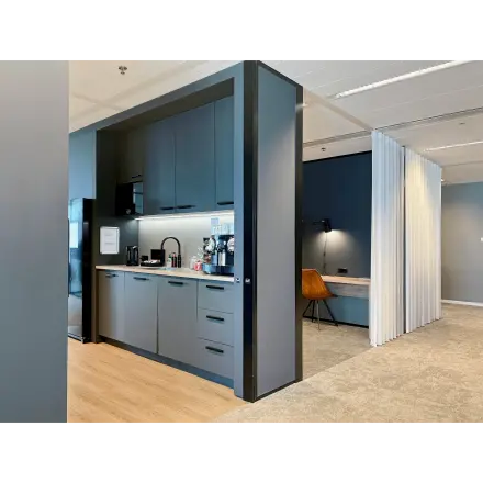 Modern office kitchen area with sleek cabinets and a coffee machine located in Rotterdam Kop van Zuid. Adjacent workspace for office space rental.