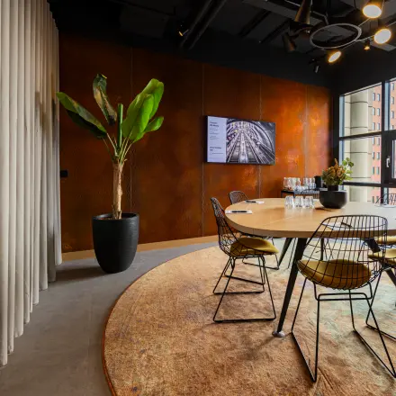 Modern office space at Wilhelminaplein 1-40, Rotterdam Kop van Zuid with a round wooden table, stylish chairs, large windows, and a potted plant, available for office space rental.
