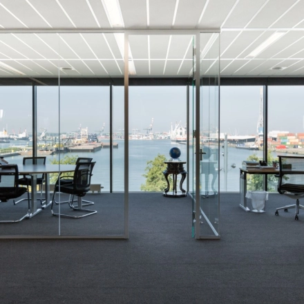 Modern office space rental at Waalhaven O.z. 83, Rotterdam Waalhaven, featuring expansive glass walls with harbor views and sleek furnishings in a meeting area.