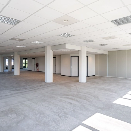 Open and spacious office interior in Schiedam with large windows allowing natural light, ideal for office space rental. Neutral grey flooring and white walls offer a versatile setup for businesses.