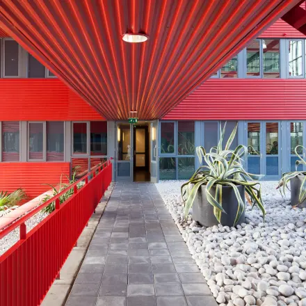 A vibrant red exterior hallway at Schiphol Airport's Folkstoneweg office to rent, featuring large potted plants and modern architectural design.