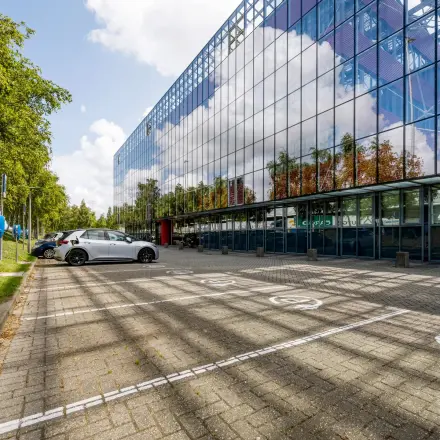 Exterior view of an office building at Folkstoneweg 2-56, Schiphol Airport, featuring reflective glass windows and adjacent parking spaces, highlighting opportunities for office space rental.