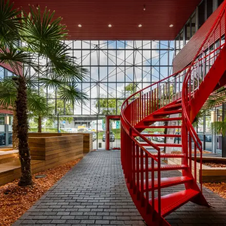 Bright office space in Schiphol Airport with a striking red spiral staircase and indoor greenery.
