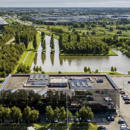 Aerial view of a modern office building surrounded by greenery and water at Schiphol Airport.
