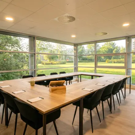 Spacious office with large windows overlooking greenery at Boeing Avenue 1-19, perfect for office space rental. Modern furnishings include a large table and chairs, ideal for meetings.