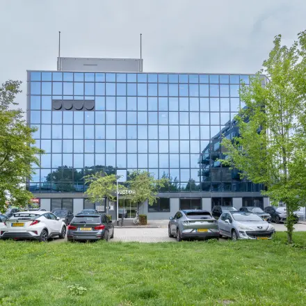 Exterior view of office space rental at Curieweg 9, Spijkenisse with a modern glass facade and parked cars in front.