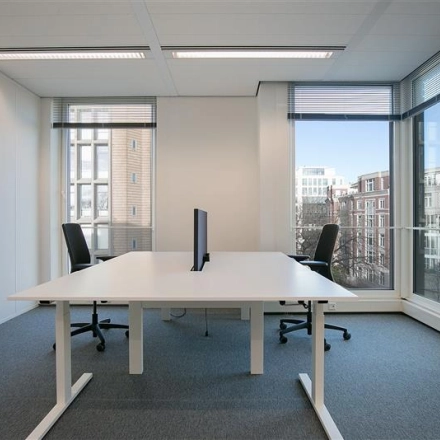 Modern office space rental at Alexanderveld 5-9, The Hague Center, featuring a bright workspace with large windows, two desks, and chairs, ideal for professional collaboration.