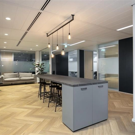 Modern office interior at Alexanderveld 5-9, The Hague, featuring a stylish open floor plan with a central table, sleek lighting, and ample seating, ideal for office space rental.