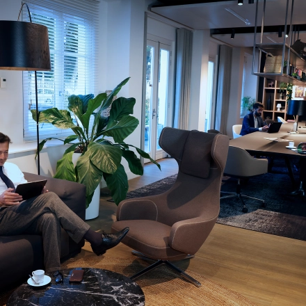 Modern office lounge with individuals working on laptops, featuring comfortable seating and stylish decor, located at Koninginnegracht 19 in The Hague Center, available for office space rental.
