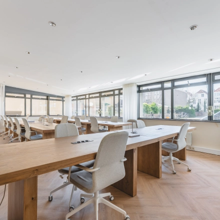 Bright office space at Zeestraat 100, The Hague Center, featuring large windows and wooden desks, ideal for office space rental.