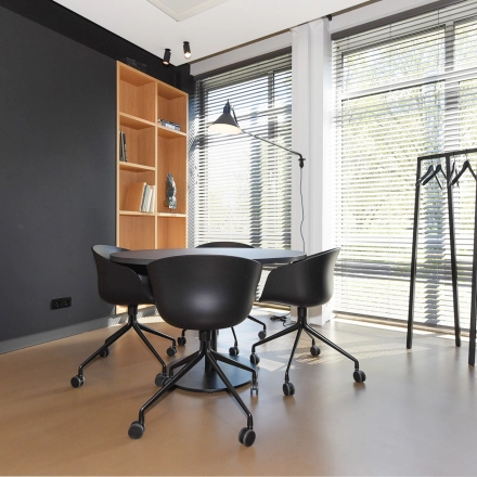 Furnished office space with a small round table and chairs, bookshelf, coat rack, and a window with blinds for rent at President Kennedylaan 19, The Hague Statenkwartier.