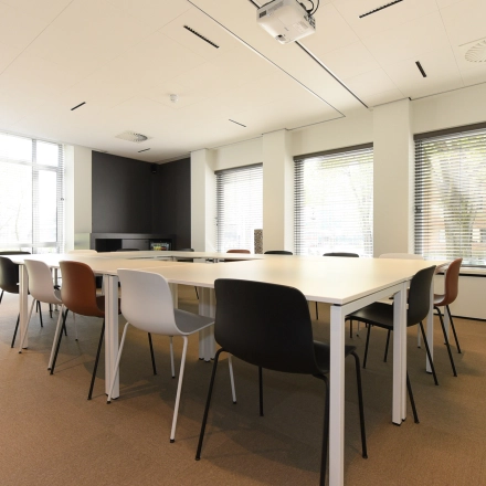 Bright office space rental in The Hague's Statenkwartier at President Kennedylaan 19, featuring a large meeting table and modern furnishings with natural light streaming through wide windows.