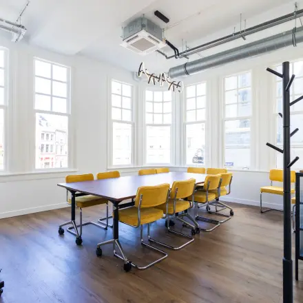 Bright office space for rent at Oudegracht 161, Utrecht Center, featuring a wooden table and yellow chairs, ideal for collaborative meetings.