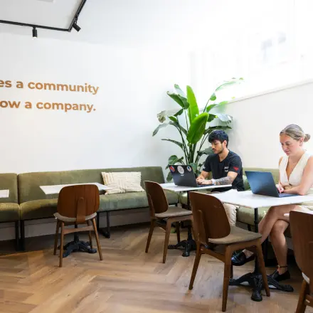 Office space at Oudegracht 161 in Utrecht Center with people working at tables, laptops open, modern decor featuring green seating and plants, ideal for office space rental.
