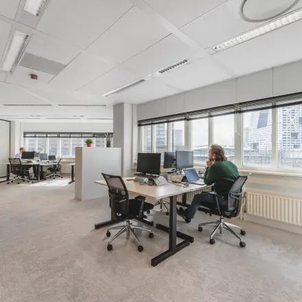 Office space at Utrecht Central Station with large windows, modern furniture, and professionals working at desks. Ideal for those seeking office space rental.