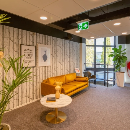 Bright office lounge at Atoomweg 400 with a cozy yellow sofa and a coffee table, ideal for office space rental in Utrecht Lage Weide.