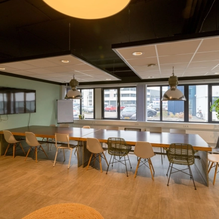 Spacious meeting room at Atoomweg 400 in Utrecht Lage Weide, featuring a large table with chairs, ideal for office space rental and collaborative work. Modern lighting and a wall-mounted screen enhance functionality.