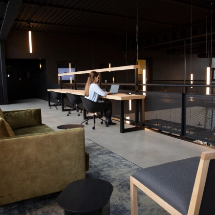 Modern office space rental at Atoomweg 63, Utrecht Lage Weide, featuring a stylish open floorplan with cozy seating and workstations where a person is working on a laptop.