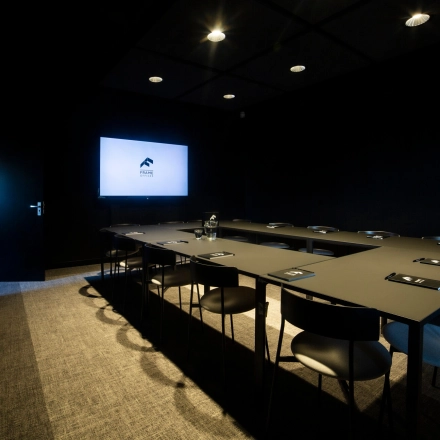 Dark, modern conference room with a large screen and neatly arranged chairs and tables, ideal for office space rental at Atoomweg 63, Utrecht Lage Weide.