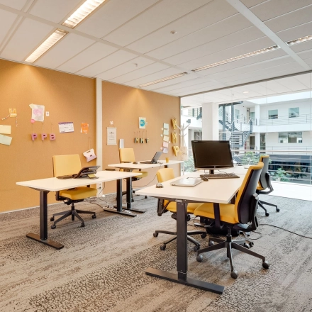Bright office space with desks, chairs, and computers, suitable for office space rental at Computerweg 22, Utrecht Lage Weide, featuring a view of the indoor atrium.