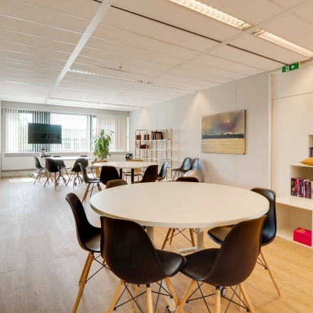 Modern office space for rent in Utrecht Lage Weide at Computerweg 22, featuring round tables, black chairs, and a wall-mounted TV, ideal for collaborative work.