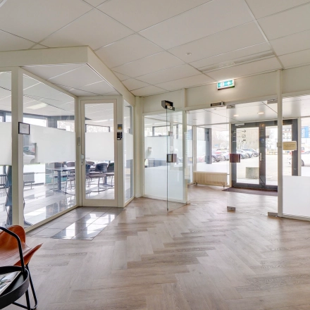 Bright office space at Zonnebaan 18, Utrecht Lage Weide with glass walls and wooden flooring, featuring a few chairs and a plant, ideal for office space rental.