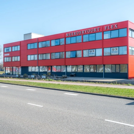 Exterior view of the office building located at Zonnebaan 18, Utrecht Lage Weide. The red facade stands out against a clear blue sky, perfect for office space rental.
