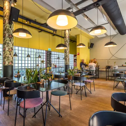 Furnished office space at Goeman Borgesiuslaan 77 in Utrecht North with tables and chairs, plants, and people in conversation. Ideal for office space rental.