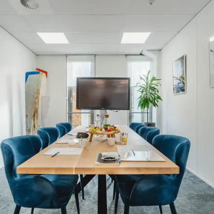 Bright office space rental at Orteliuslaan 850, Utrecht Papendorp, featuring a furnished conference room with a modern table, blue chairs, a large screen, and natural light through large windows.