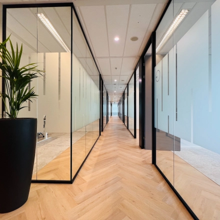 Spacious office corridor with sleek glass partitions and potted plant, located at Vliegend Hertlaan 15 in Utrecht South, suitable for office space rental.