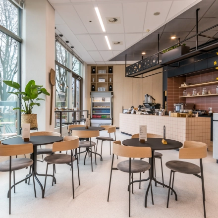 Furnished office space with modern decor and seating in Utrecht South, featuring a counter and several chairs and tables near large windows.