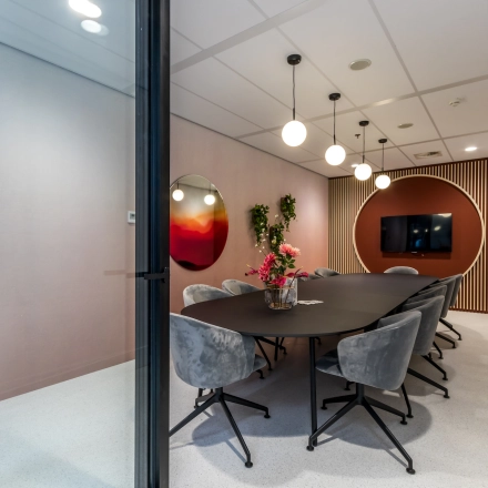 Modern conference room with a long table and stylish chairs, ready for office to rent in Utrecht South. Includes a TV screen and decorative elements.