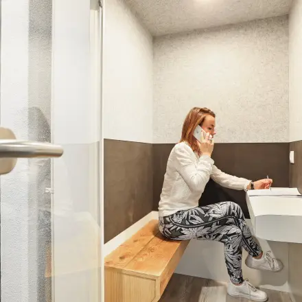 Compact call booth at Winthontlaan 200 in Utrecht South, featuring a bench, table, and a person taking a business call. Ideal for office space rental.