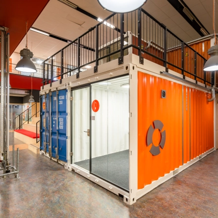 Vibrant office space interior at Proostwetering 41, Utrecht West, featuring a unique industrial design with shipping containers and bright orange accents. Ideal for office space rental, showcasing a creative and dynamic working environment.