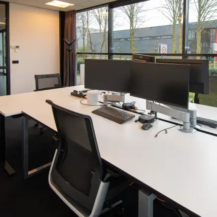 Modern office space at Gildestraat 13, Velp, featuring a sleek workspace with multiple monitors and large windows overlooking greenery, available for office space rental.