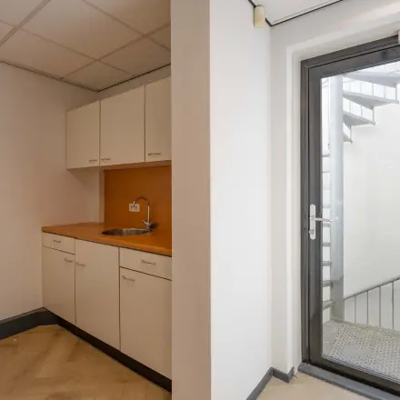Simple office pantry at Keizersveld 47 in Venray, available for rent; features a small kitchenette with cabinets and sink next to a glass door leading outside.